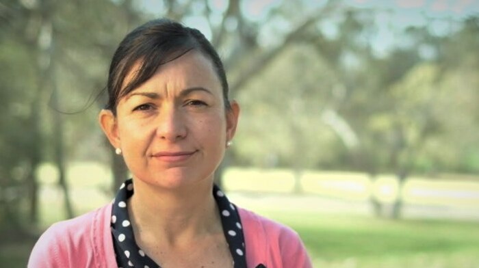 A woman stands in a park in front of trees