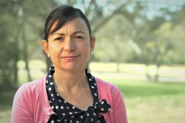 A woman stands in a park in front of trees