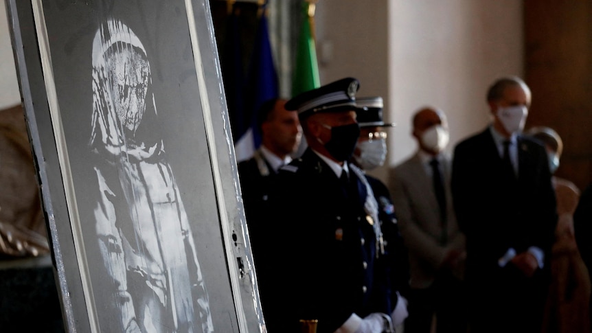 Police and officials stand next to an artwork that depicts a veiled, mournful female figure