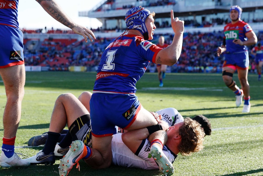 While sitting on top of an opponent, Kayln Ponga points his right index finger up while looking at the referee.