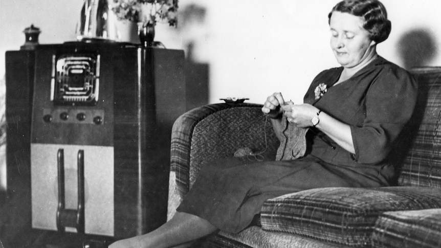 Black and white photo of a woman listening to the radio and knitting.