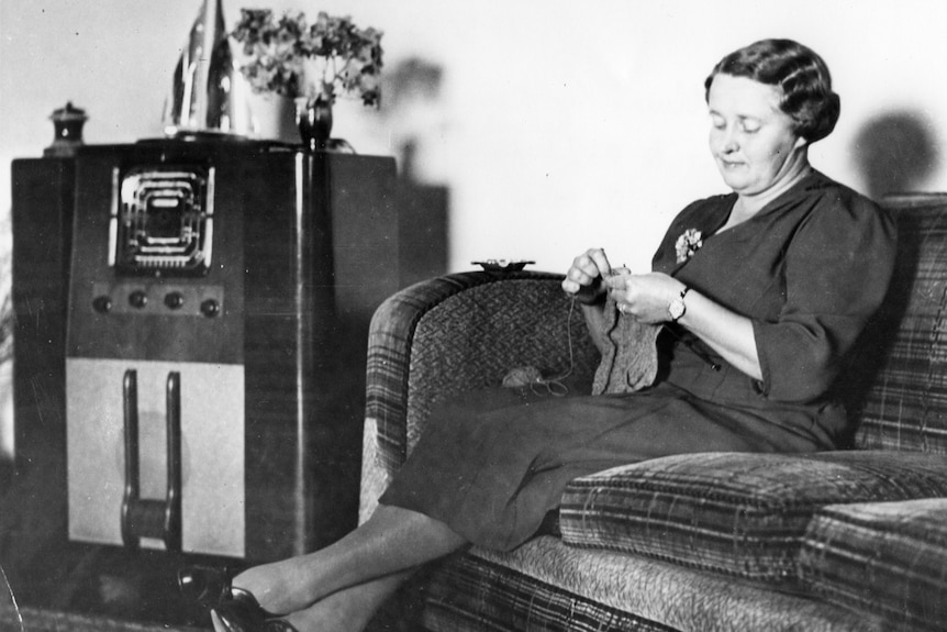 Black and white photo of a woman listening to the radio and knitting.