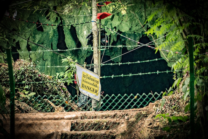 A sign that reads 'danger' and shows some Thai script is shown behind a barbed wire fence.