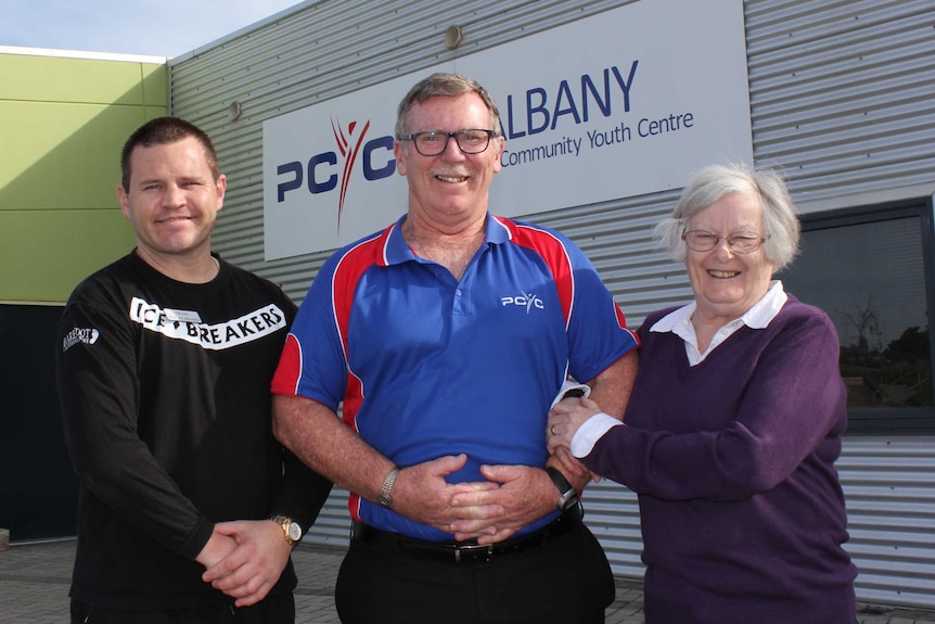 Two men and a woman stand together outside a PCYC building.