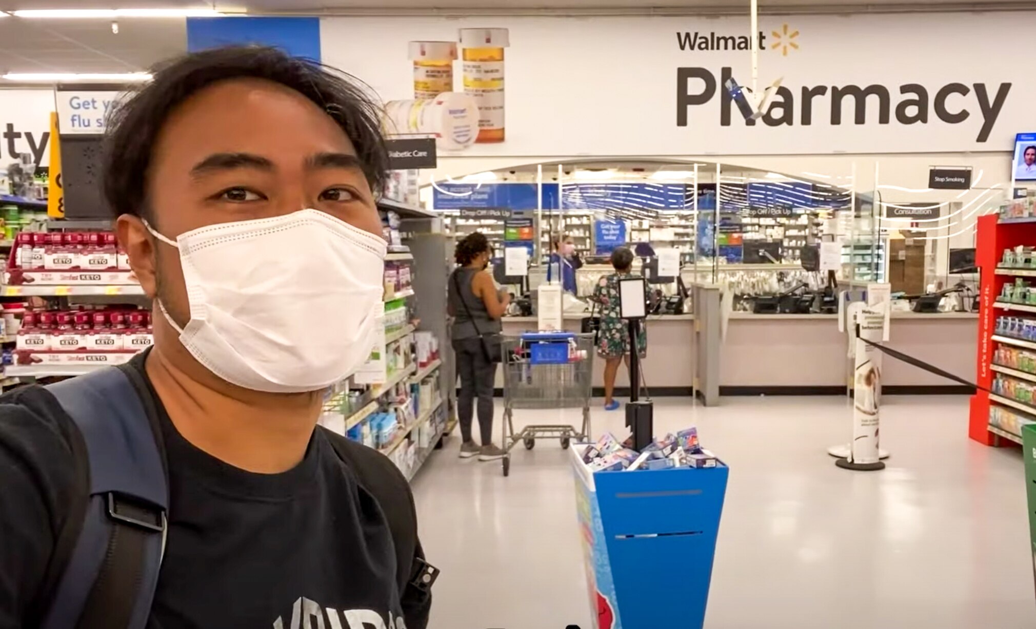 A young Thai man in a white face mask takes a selfie at a Walmart pharmacy
