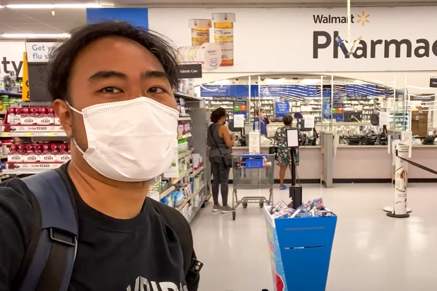 A young Thai man in a white face mask takes a selfie at a Walmart pharmacy