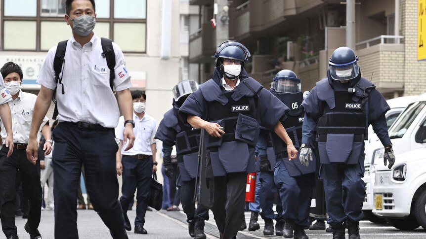 Police wearing protective gear and helmets walk along a street.