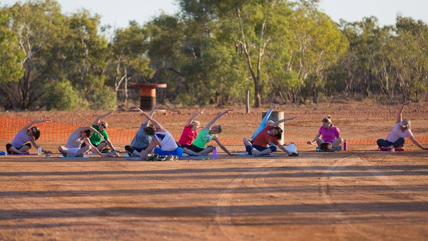 Women sit in red dirt doing exercises