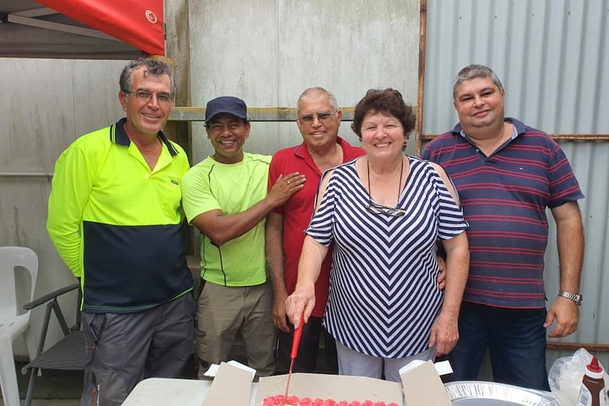 five people stand around a cake smiling at the camera