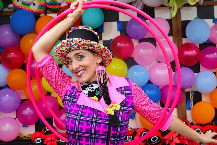 Woman wearing circus costume in front of balloon wall holding hula hoops. 