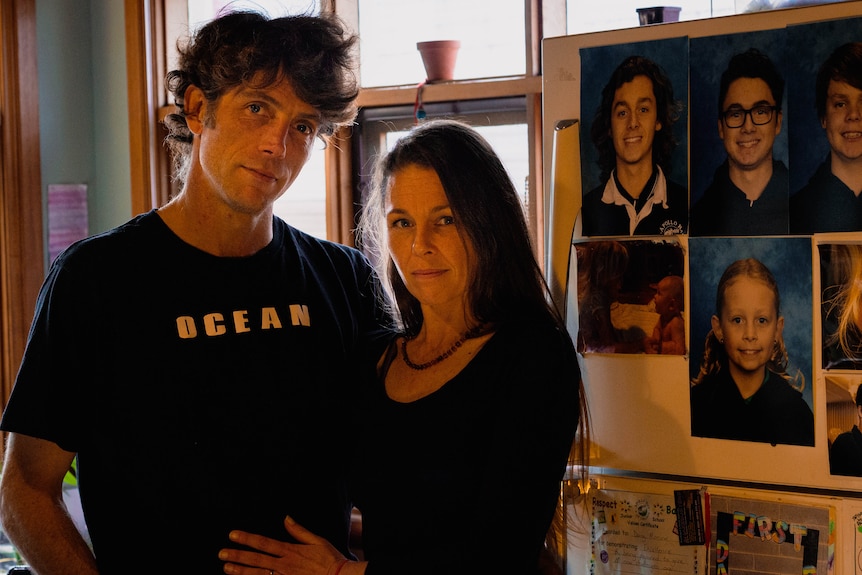 A man and woman stand next to photos of their kids on the fridge