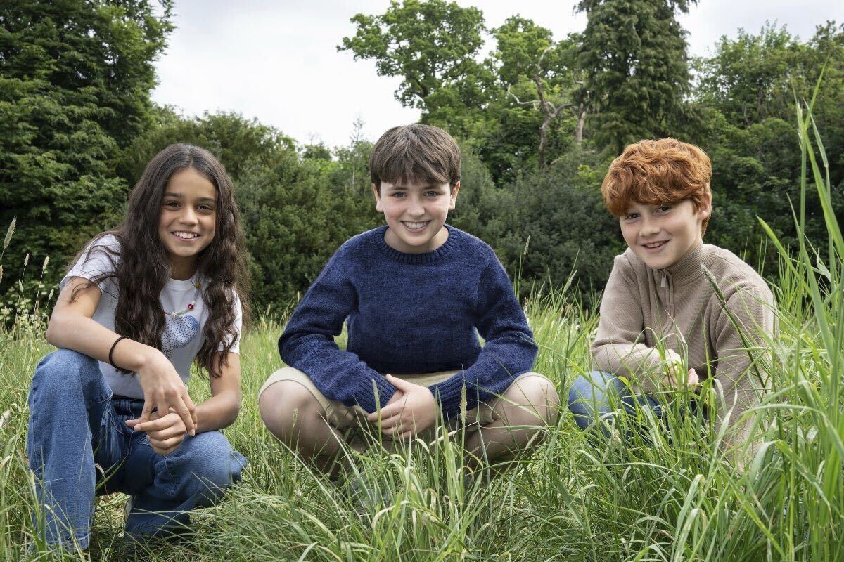 Three children crouch in long grass and smile