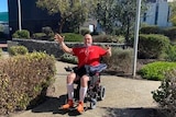 man in red tshirt sitting in wheelchair giving both thumbs up