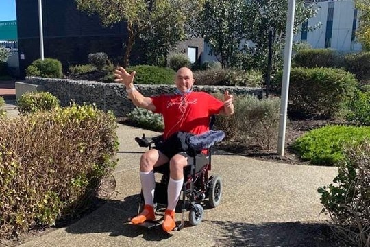 man in red tshirt sitting in wheelchair giving both thumbs up