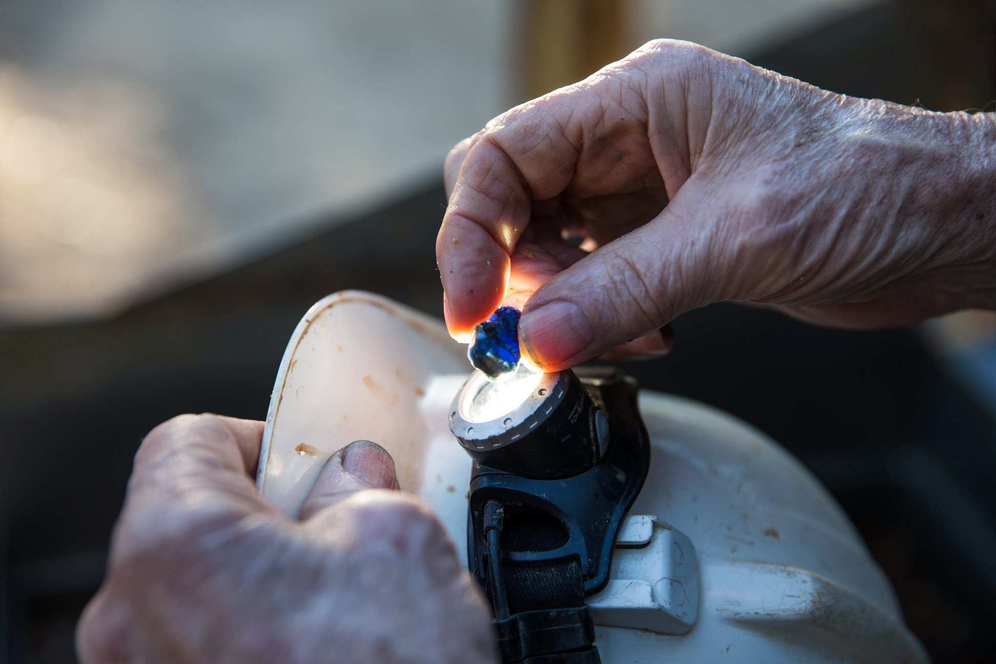 A close up of a hand holding a blue sapphire stone to the light of a torch.