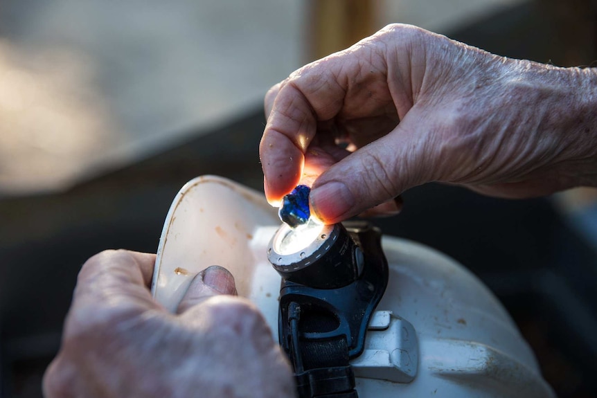 A close up of a hand holding a blue sapphire stone to the light of a torch.