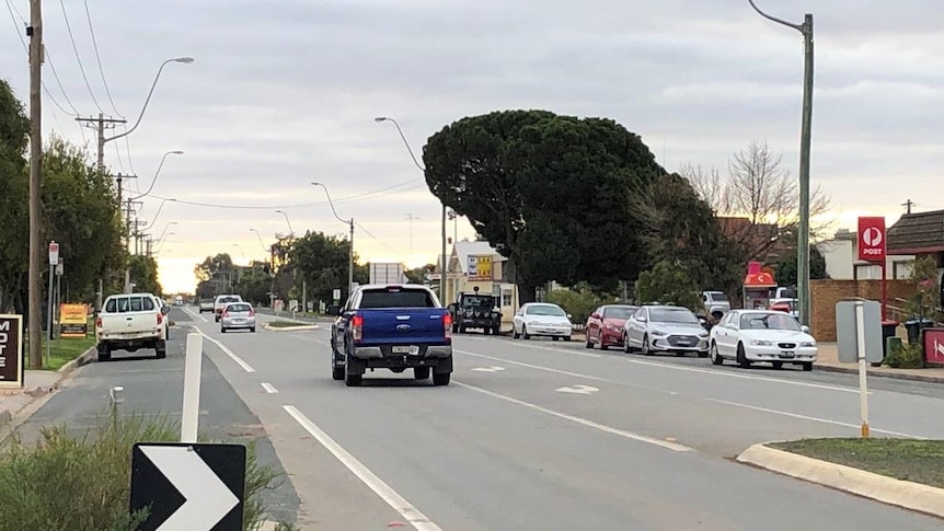 A blue ute and other vehicles travelling down the main street of Balranald on a cloudy day.