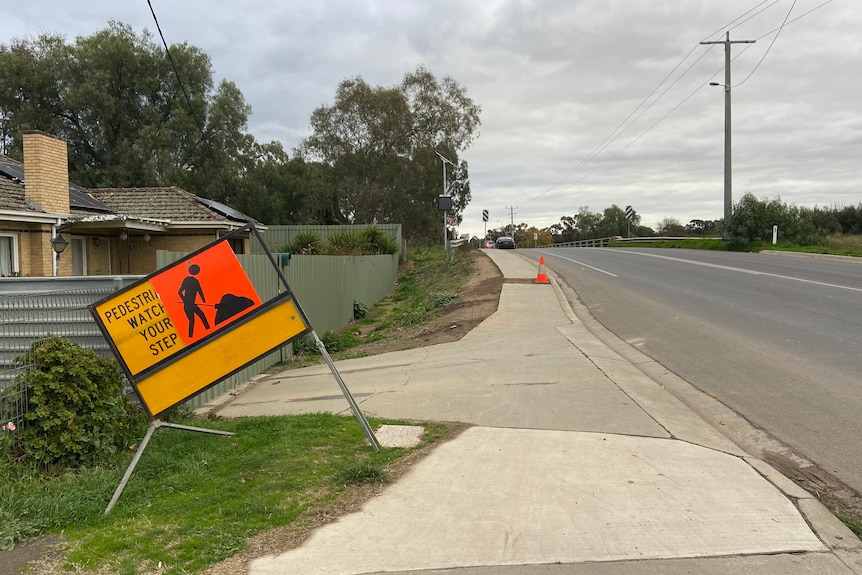 A roadwork sign and uneven footpath on Howard St near a bridge.