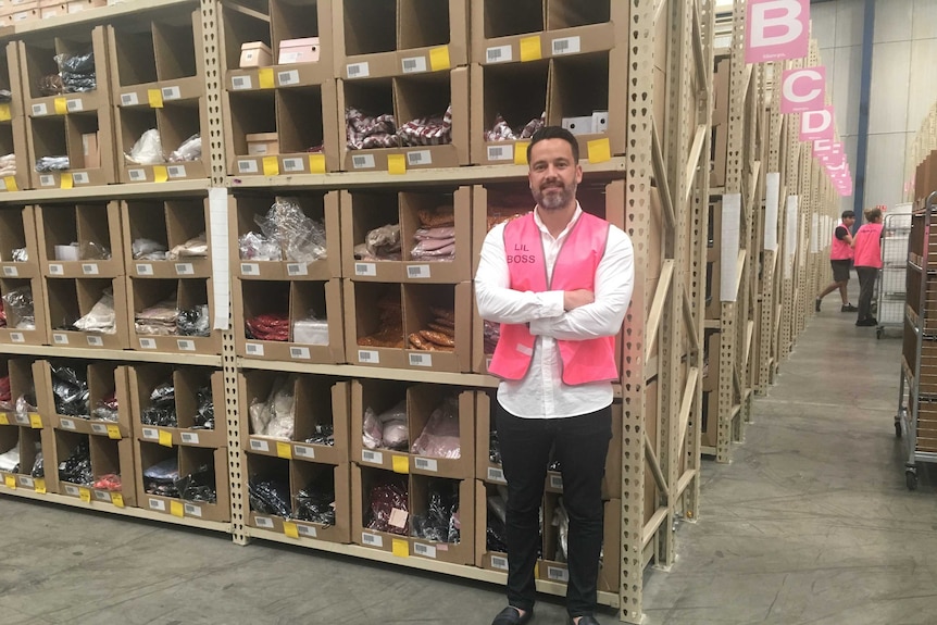 Paul Waddy standing in front of shelves in a warehouse wearing a pink high-vis vest.