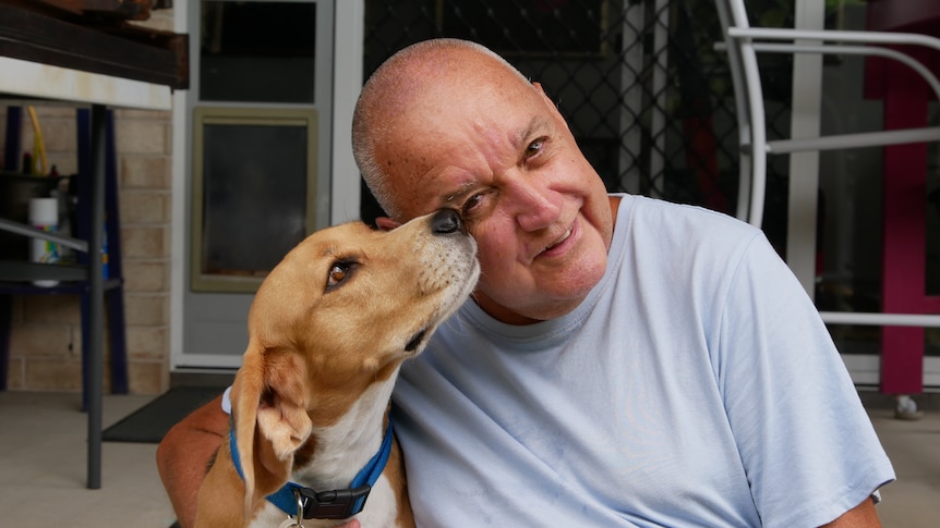 A man sits on his back porch and pets his dog.