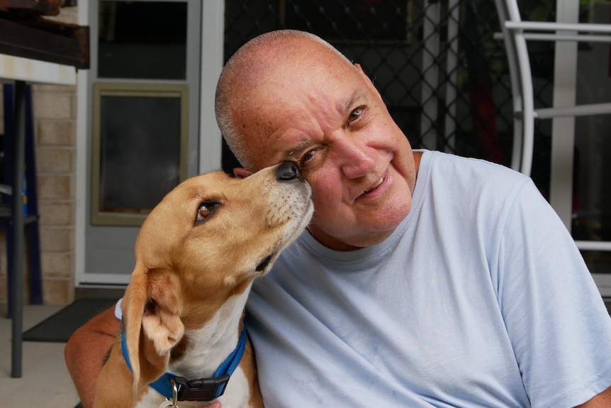 A man sits on his back porch and pets his dog.