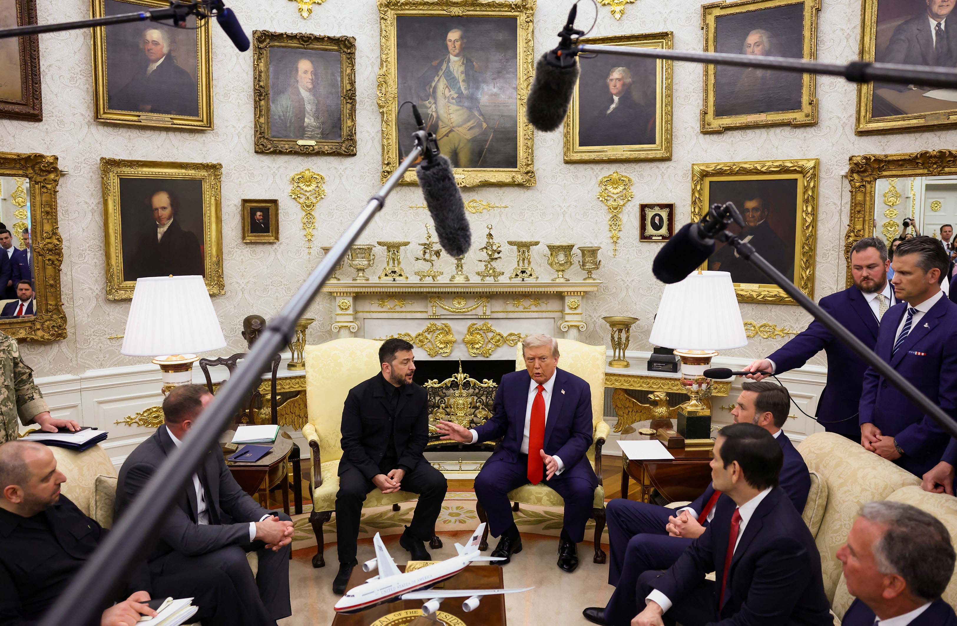 Media with cameras surround Trump and Zelenskyy who are sitting on chairs in the oval office
