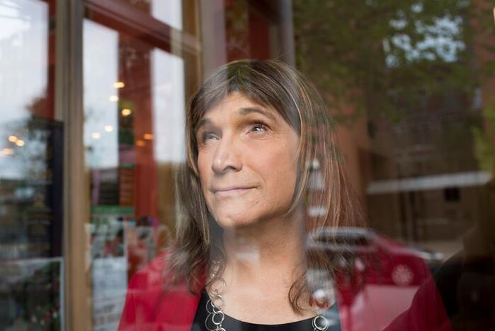 Christine Hallquist amiles as she looks through a glass window