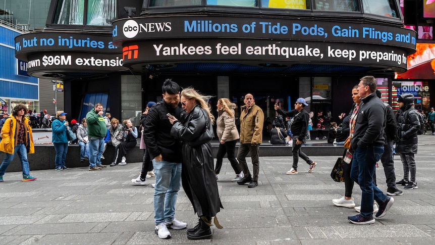 People stand at Times Square where news tickers dispaly news on an earthquake