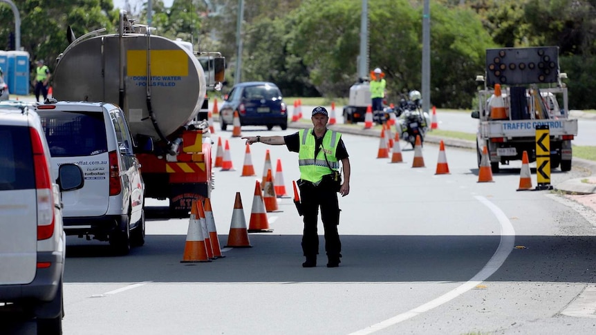 A police officer at a checkpoint directs motorists lined up at Queensland-NSW border at Coolangatta.