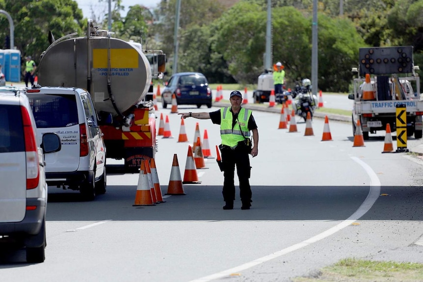 Un ufficiale di polizia a un posto di blocco dirige gli automobilisti in fila al confine del Queensland e del Nuovo Galles del Sud a Coolangatta.