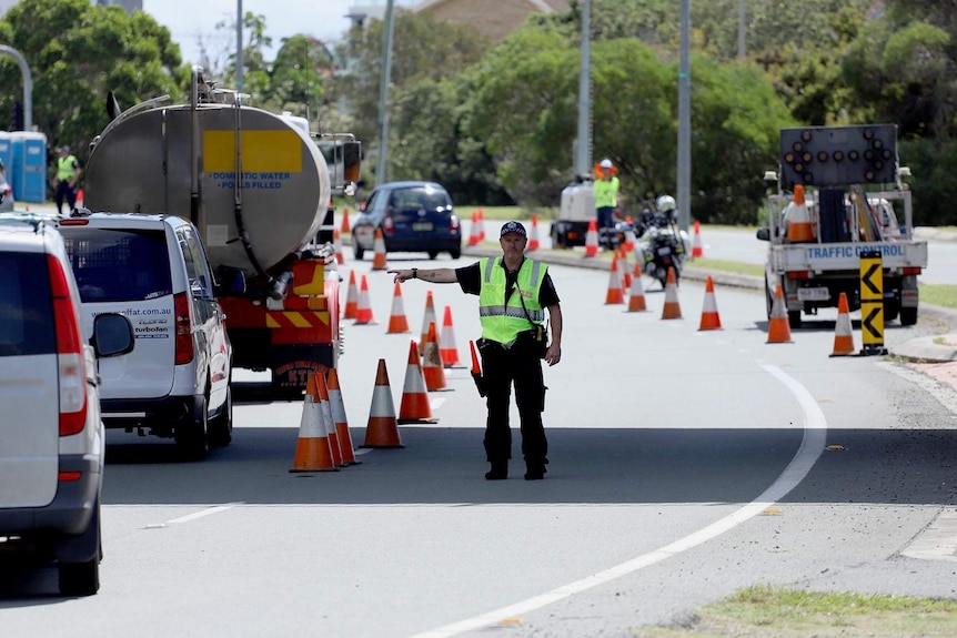 A police officer at a checkpoint directs motorists lined up at Queensland-NSW border at Coolangatta.