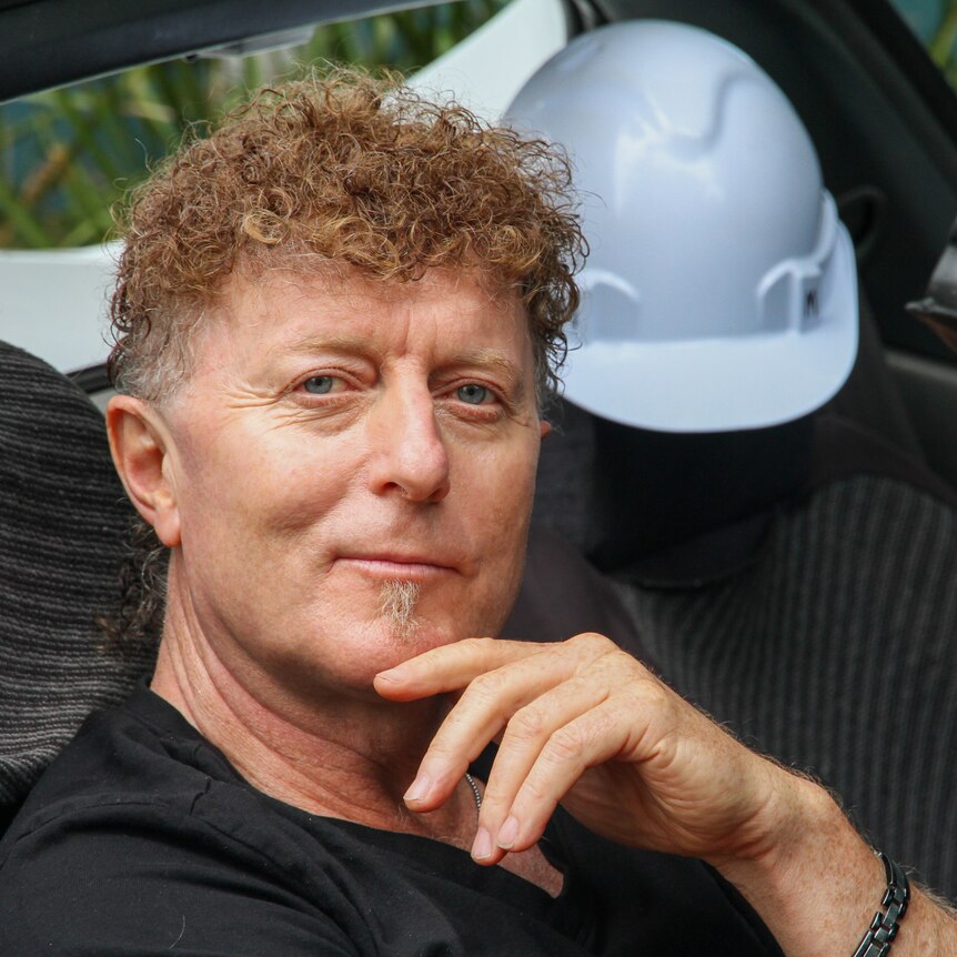 A man with curly hair sitting in a car.