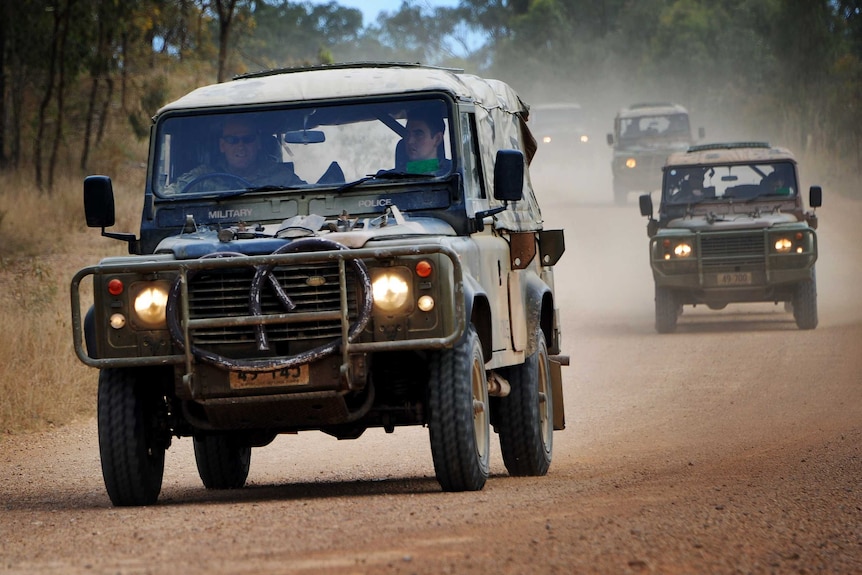 Australian Army Landrover 110s travel in convoy down a dirt road.
