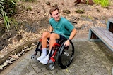 A man in a wheelchair pictured pictured smiling outdoors.