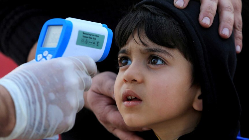 A boy in a black hoodie jumper looks at a blue and white thermometer being held by a hand in a rubber glove.
