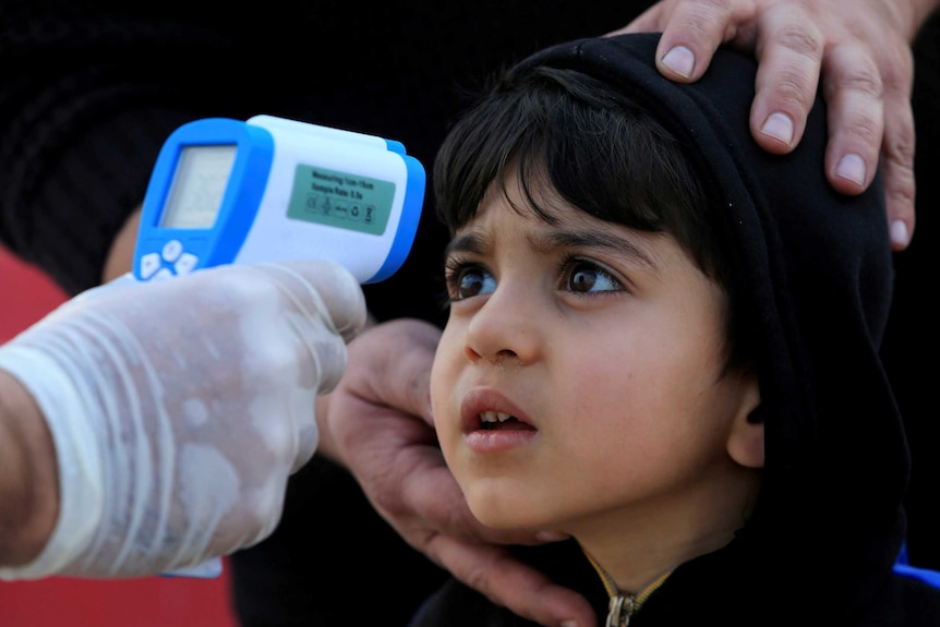 A boy in a black hoodie jumper looks at a blue and white thermometer being held by a hand in a rubber glove.