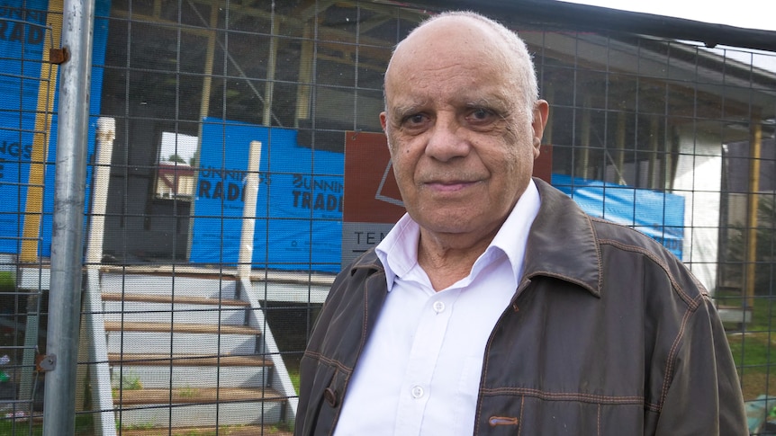 Portrait of man with gentle smile standing in front of a small cottage under construction