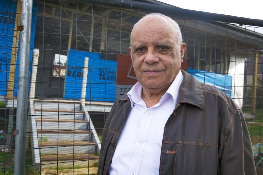 Portrait of man with gentle smile standing in front of a small cottage under construction