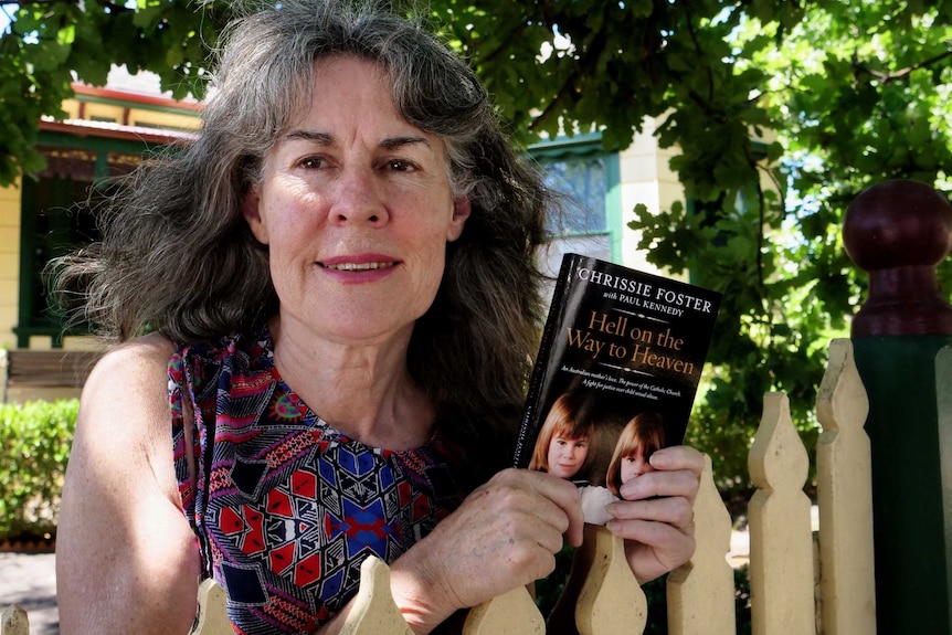 Chrissie Foster leans against a picket fence with her book, Hell on the Way to Heaven.