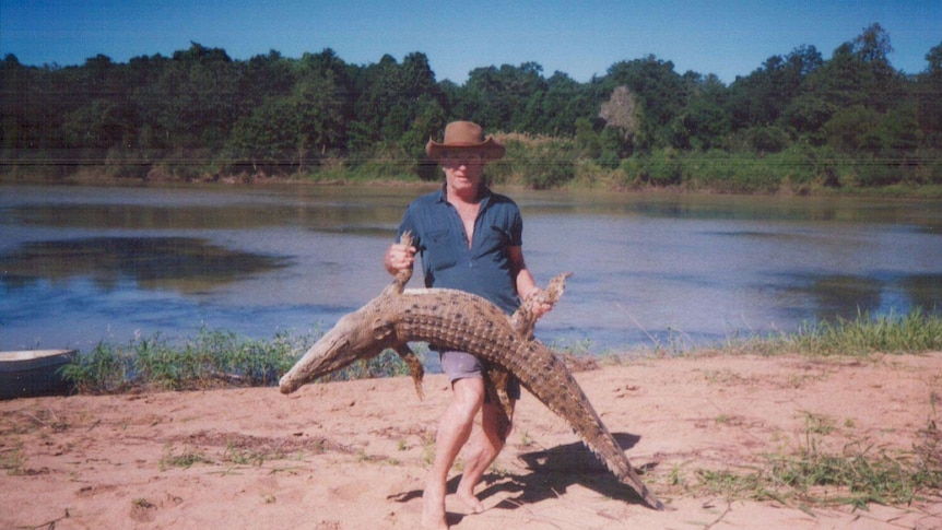An older Bill Dean holds a crocodile by a river bank