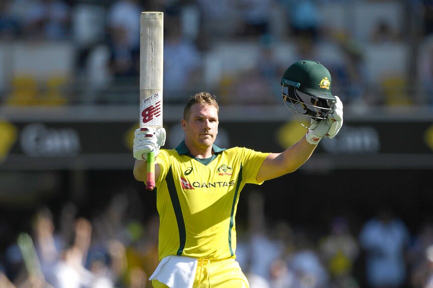Aaron Finch holds his bat and helmet aloft in celebration of scoring a century.