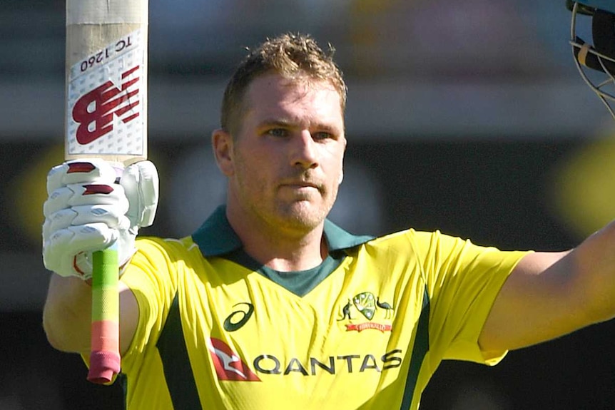 Aaron Finch holds his bat and helmet aloft in celebration of scoring a century.