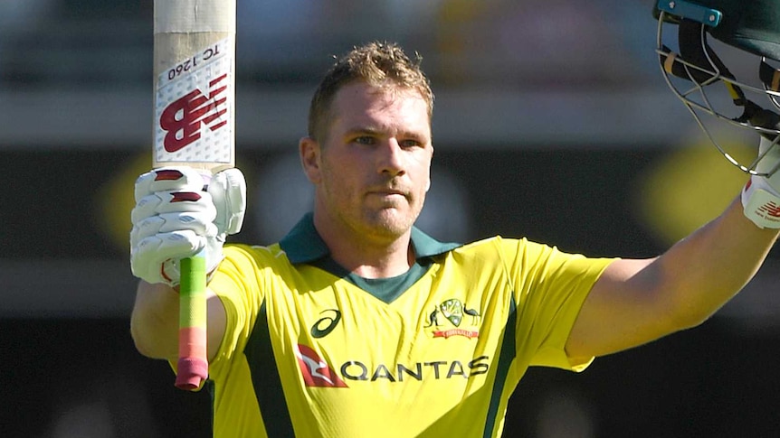 Aaron Finch holds his bat and helmet aloft in celebration of scoring a century.