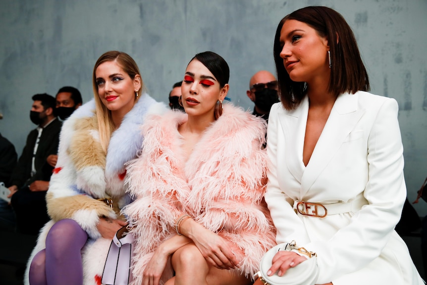 Three women sit in the front row of a fashion show 