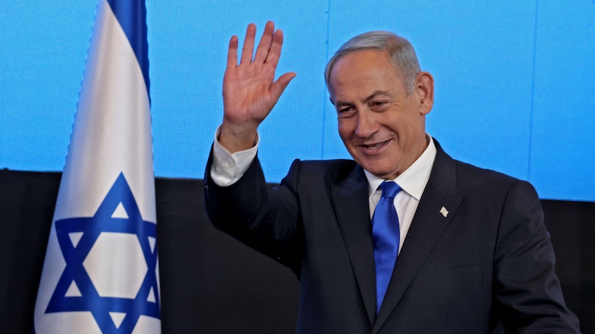 Benjamin Netanyahu stands and waves next to Israel flag on left