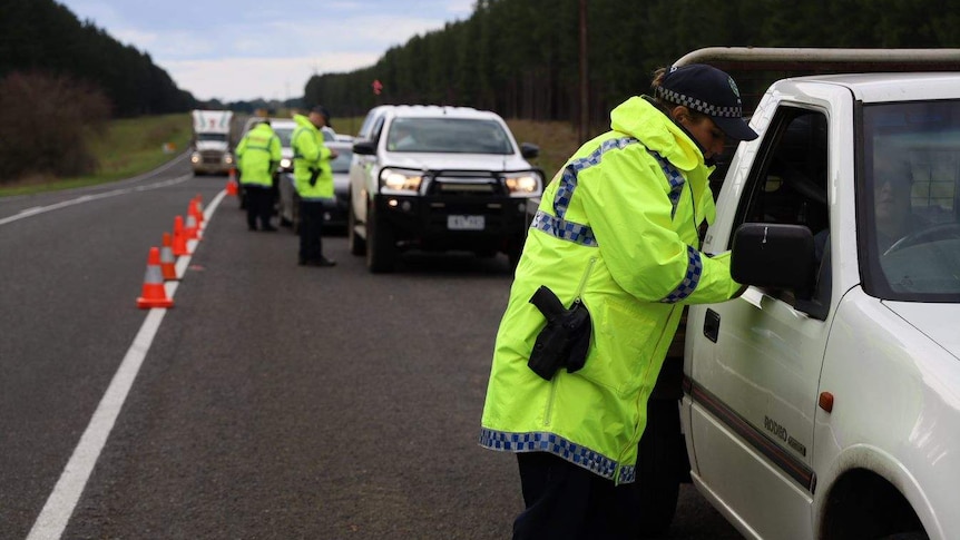 Police in hi-vis patrol a border checkpoint along a highway.