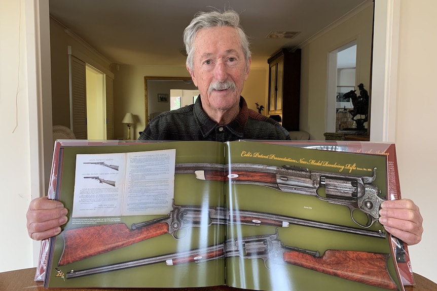 A man holding  a book open to a page showing images of guns.