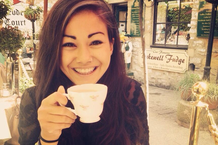 A girl smiles big with a cup of tea in her hand