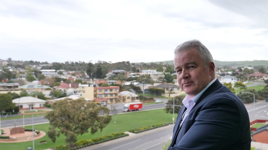 A man dressed in a suit standing on a balcony overlooking Port Lincoln.