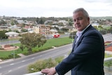 A man dressed in a suit standing on a balcony overlooking Port Lincoln.